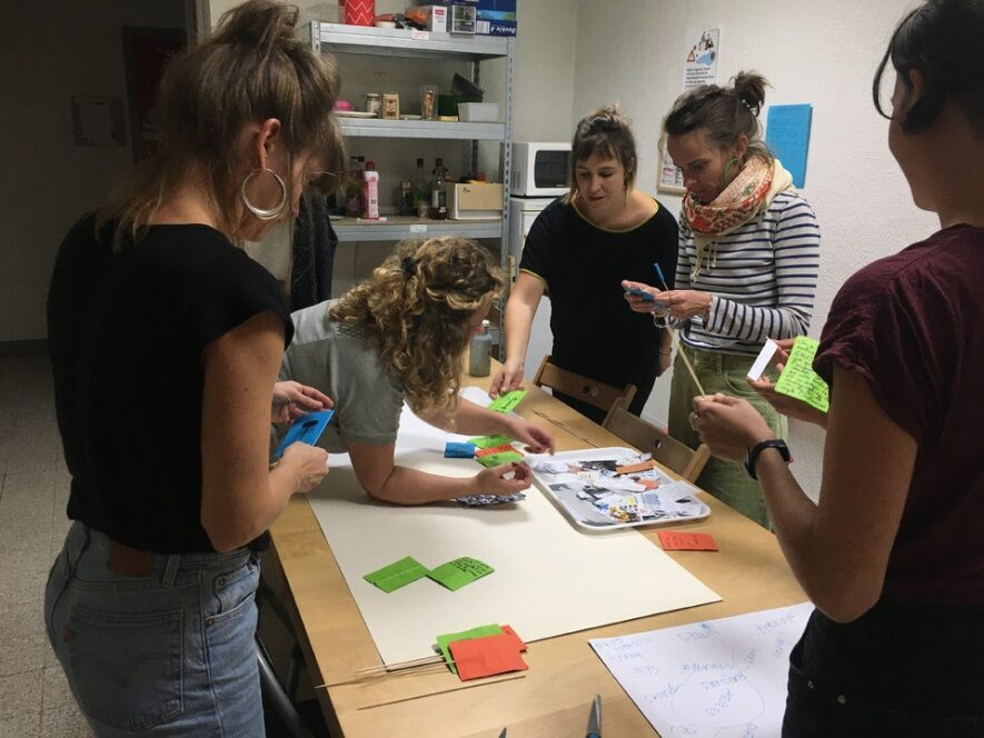 5 femmes en train de découper et coller des cartons de couleurs avec des choses écrites dessus